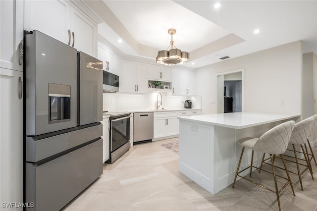 kitchen featuring a peninsula, a sink, white cabinetry, appliances with stainless steel finishes, and a raised ceiling