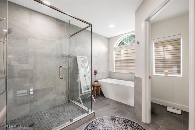 bathroom with a soaking tub, tile patterned flooring, tile walls, and a stall shower