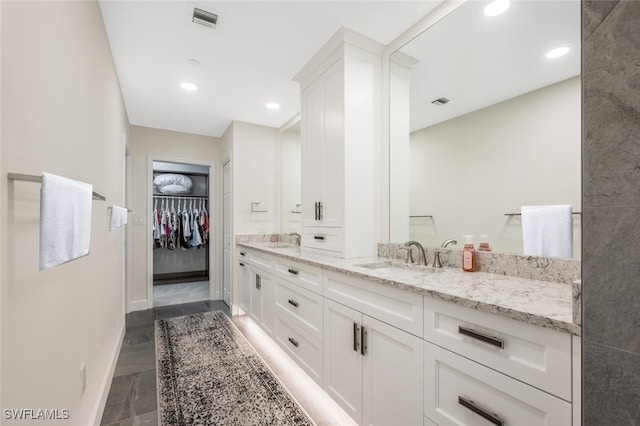 bathroom with double vanity, visible vents, a walk in closet, and a sink