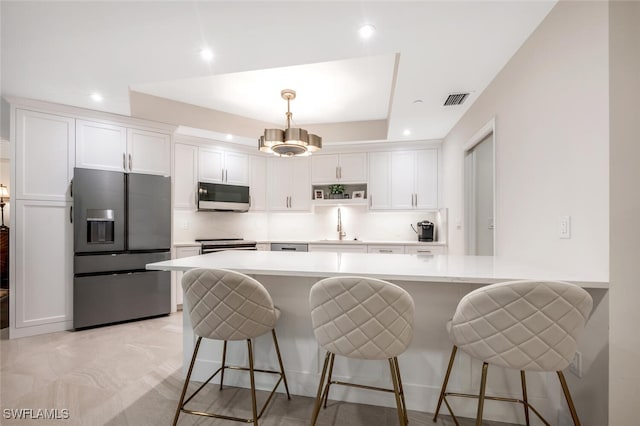 kitchen featuring appliances with stainless steel finishes, white cabinetry, visible vents, and a kitchen bar