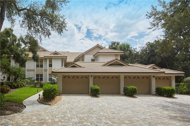 view of front facade with an attached garage, a tiled roof, decorative driveway, and stucco siding