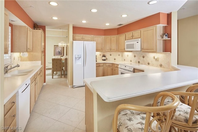 kitchen featuring light countertops, light brown cabinets, white appliances, a peninsula, and a kitchen bar