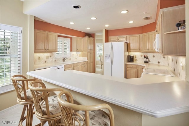 kitchen featuring a peninsula, white appliances, light countertops, and a kitchen breakfast bar