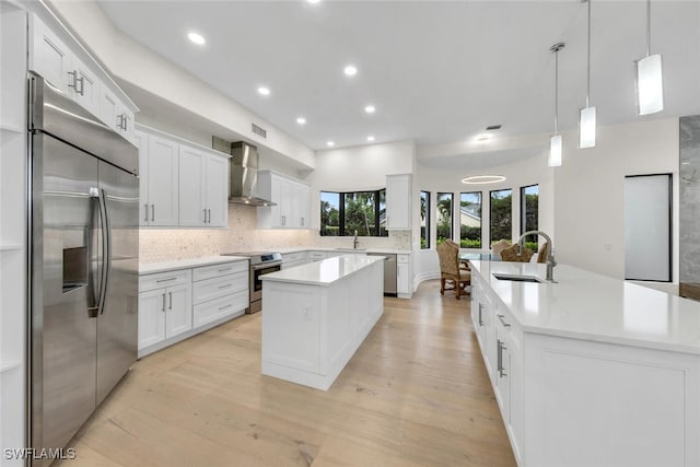 kitchen with wall chimney exhaust hood, sink, a kitchen island, and stainless steel appliances