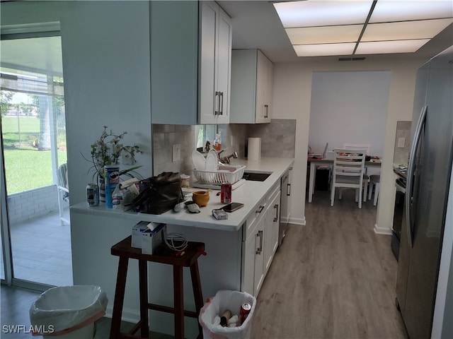 kitchen with stainless steel fridge, sink, tasteful backsplash, light hardwood / wood-style flooring, and white cabinetry