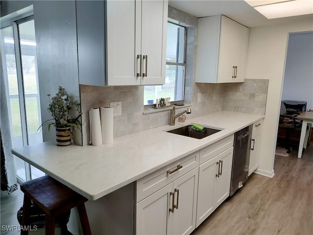 kitchen featuring sink, light wood-type flooring, black dishwasher, white cabinets, and backsplash