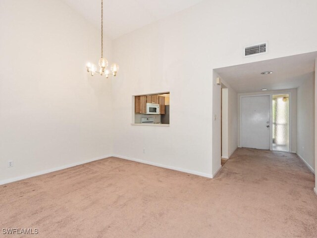 carpeted spare room featuring an inviting chandelier and high vaulted ceiling