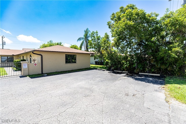 view of side of property with uncovered parking, a gate, fence, and stucco siding