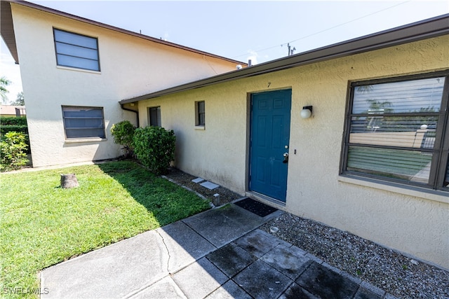 doorway to property with a lawn and stucco siding