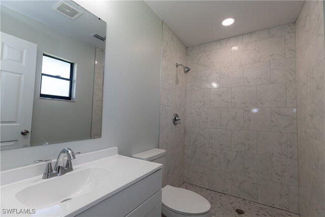 bathroom with visible vents, a tile shower, vanity, and toilet