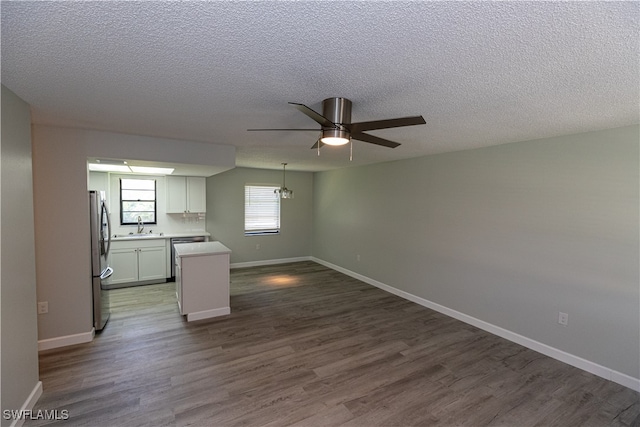 interior space with a textured ceiling, dark wood-type flooring, a sink, a ceiling fan, and baseboards