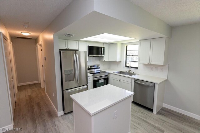 kitchen featuring sink, white cabinets, a kitchen island, light hardwood / wood-style flooring, and appliances with stainless steel finishes