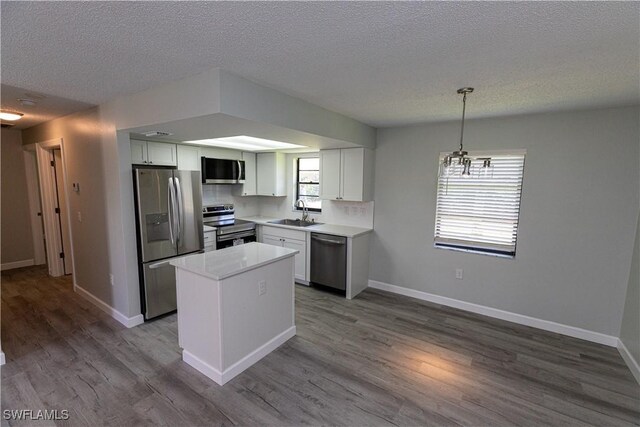 kitchen featuring wood-type flooring, a notable chandelier, white cabinets, hanging light fixtures, and stainless steel appliances