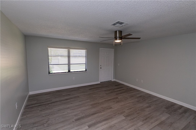 empty room with visible vents, dark wood finished floors, a textured ceiling, and baseboards