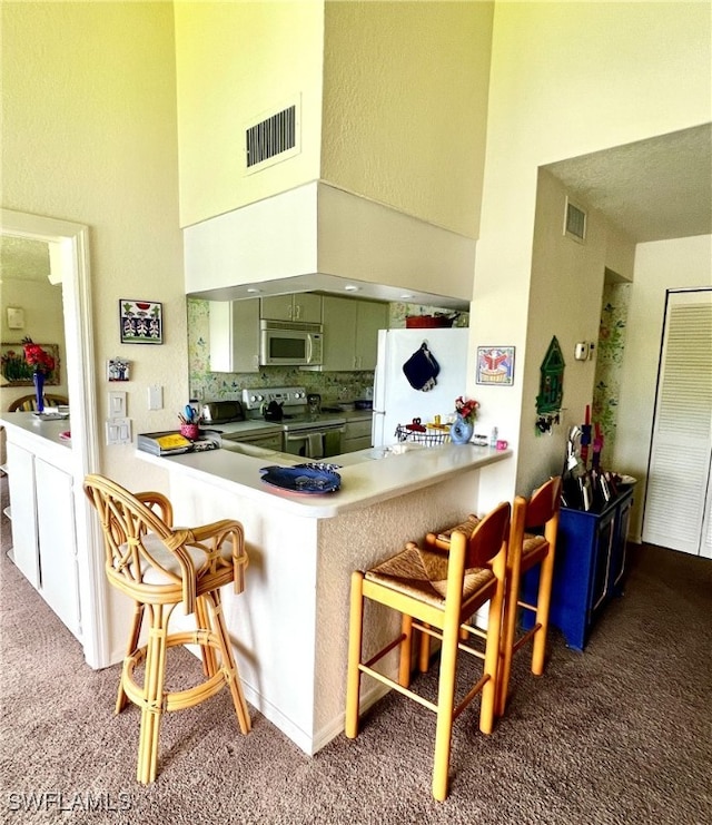 kitchen featuring kitchen peninsula, appliances with stainless steel finishes, a high ceiling, dark colored carpet, and a breakfast bar