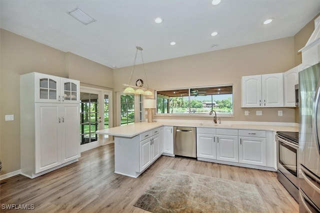 kitchen featuring pendant lighting, light wood-type flooring, white cabinets, kitchen peninsula, and appliances with stainless steel finishes