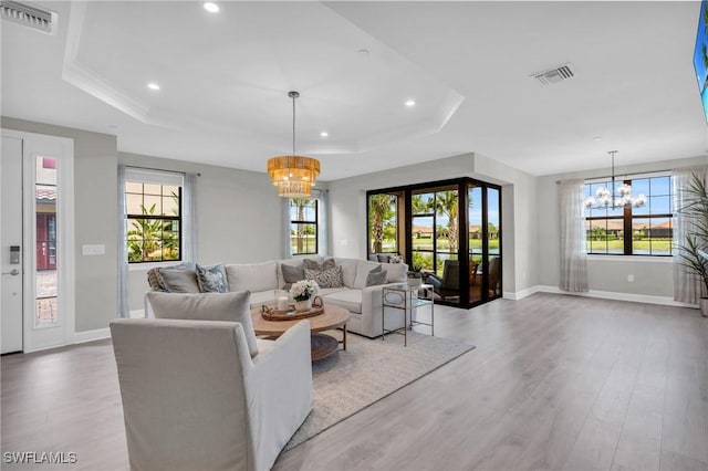 living area featuring a chandelier, a raised ceiling, visible vents, and wood finished floors