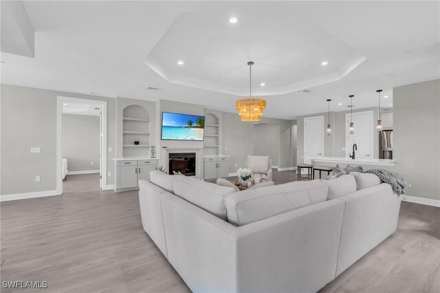 living room featuring built in shelves, light hardwood / wood-style flooring, a raised ceiling, and sink