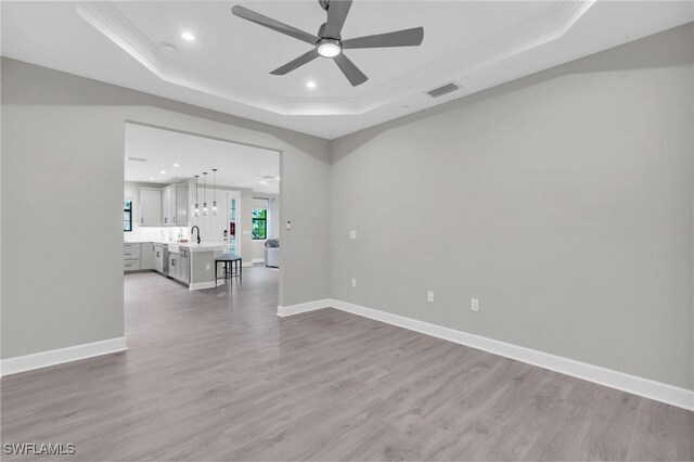 spare room featuring sink, hardwood / wood-style flooring, ceiling fan, ornamental molding, and a tray ceiling