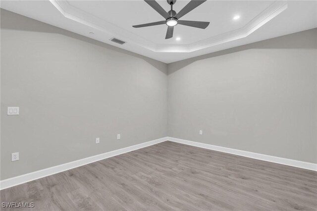 spare room with a tray ceiling, hardwood / wood-style flooring, crown molding, and ceiling fan