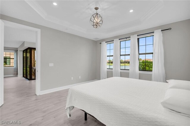 bedroom with a chandelier, light wood-type flooring, a tray ceiling, and ornamental molding