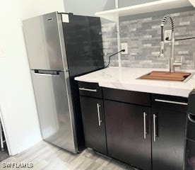 kitchen with stainless steel fridge, light hardwood / wood-style floors, decorative backsplash, and sink