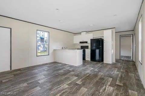 kitchen with white cabinetry, black fridge, dark hardwood / wood-style flooring, and kitchen peninsula