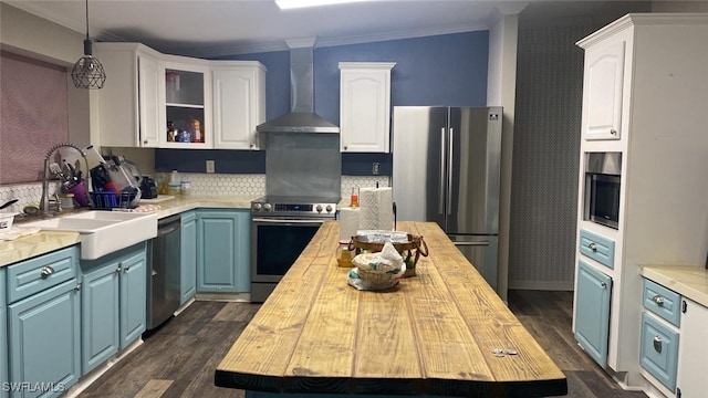 kitchen featuring sink, wall chimney range hood, appliances with stainless steel finishes, white cabinets, and blue cabinets