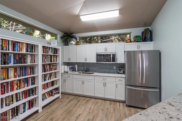 kitchen with appliances with stainless steel finishes, light hardwood / wood-style floors, white cabinetry, and light stone countertops