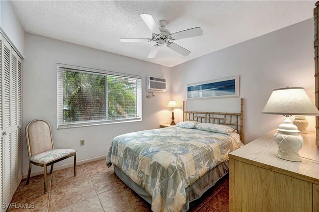 tiled bedroom with ceiling fan, a textured ceiling, a closet, and a wall unit AC