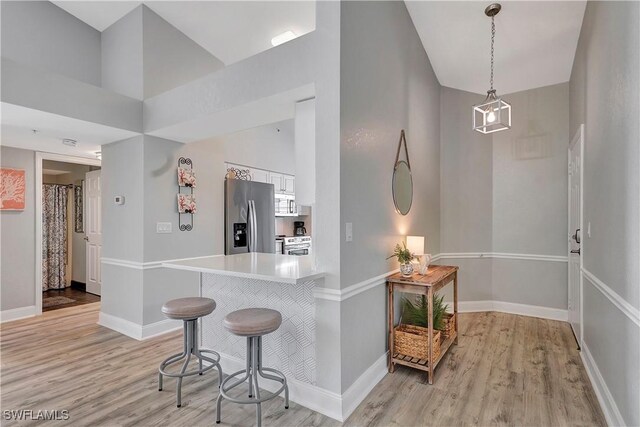 kitchen featuring a breakfast bar area, light wood-type flooring, pendant lighting, stainless steel appliances, and white cabinets