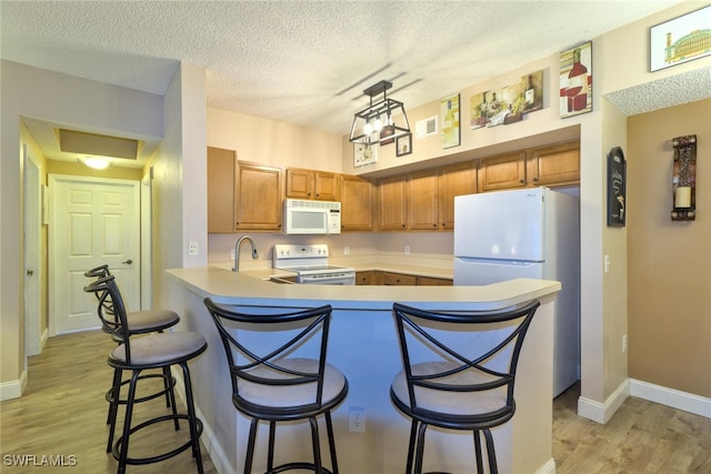 kitchen with a textured ceiling, kitchen peninsula, a kitchen bar, light hardwood / wood-style flooring, and white appliances