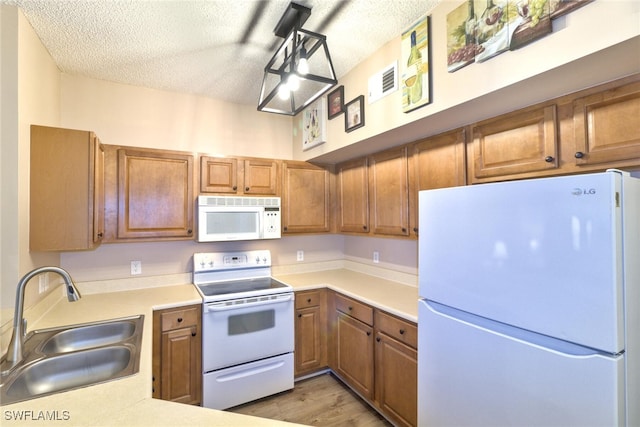 kitchen with a textured ceiling, white appliances, sink, and light hardwood / wood-style flooring