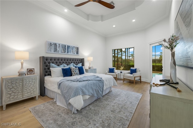 bedroom featuring a towering ceiling, light hardwood / wood-style floors, a raised ceiling, and ceiling fan