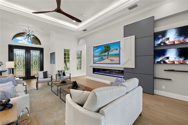 living room with a tray ceiling, french doors, ornamental molding, and light hardwood / wood-style flooring