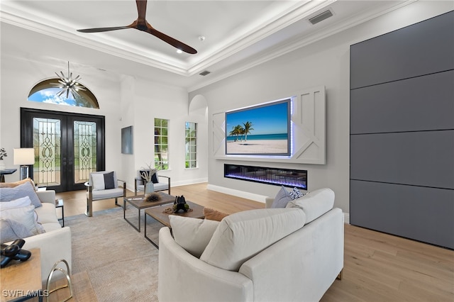 living room with a raised ceiling, crown molding, french doors, and light hardwood / wood-style flooring