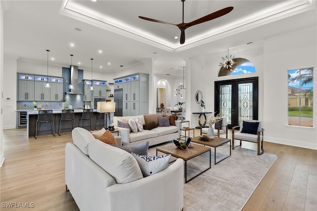 living room featuring ceiling fan, french doors, a raised ceiling, light hardwood / wood-style floors, and ornamental molding