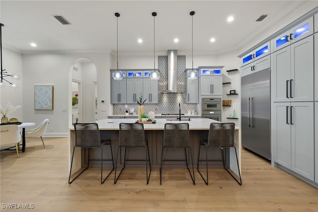 kitchen featuring a large island, hanging light fixtures, stainless steel appliances, and wall chimney range hood