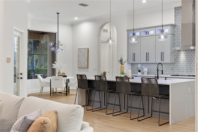 kitchen with wall chimney exhaust hood, hanging light fixtures, backsplash, a breakfast bar area, and light wood-type flooring