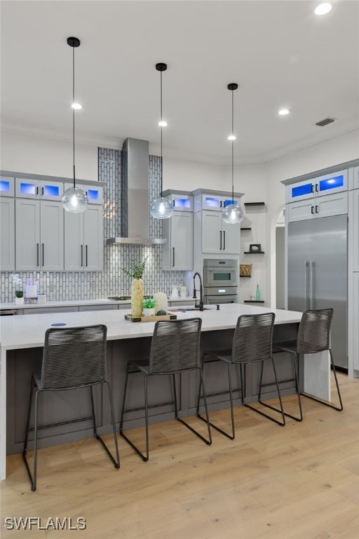 kitchen featuring wall chimney exhaust hood, a kitchen breakfast bar, a spacious island, pendant lighting, and appliances with stainless steel finishes