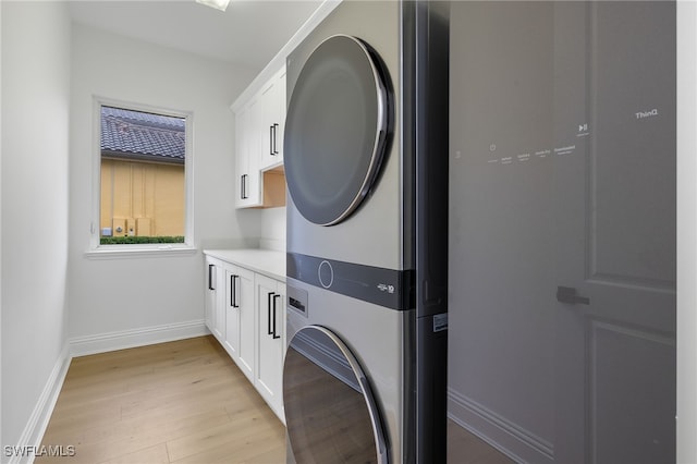 laundry area with cabinets, stacked washer and dryer, and light hardwood / wood-style floors