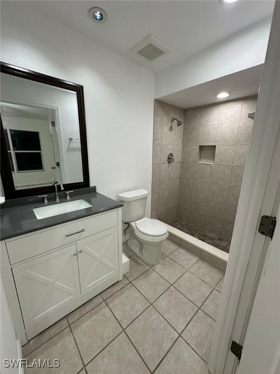 bathroom featuring a tile shower, tile patterned flooring, vanity, and toilet