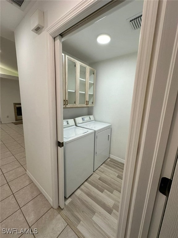 clothes washing area featuring cabinets, independent washer and dryer, and light hardwood / wood-style flooring