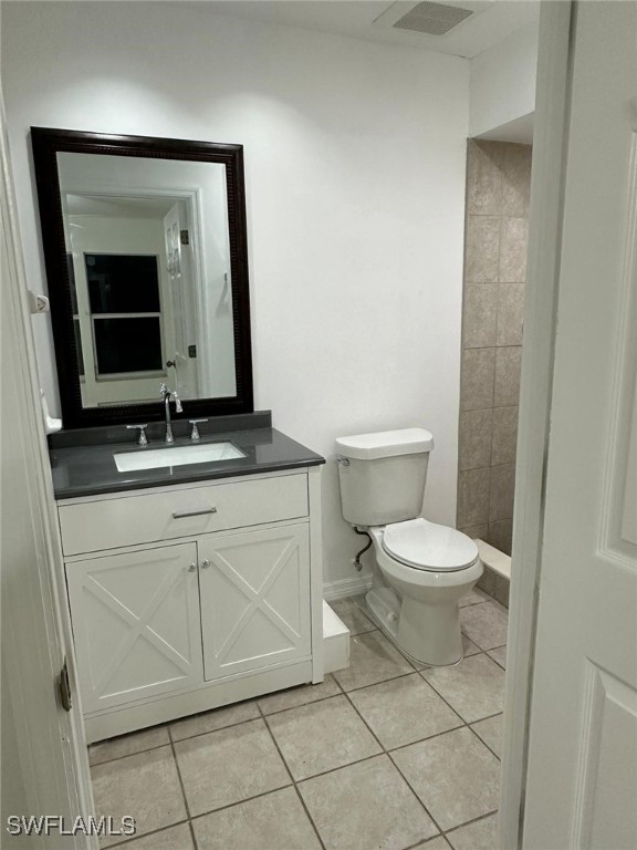 bathroom with a tile shower, vanity, toilet, and tile patterned floors