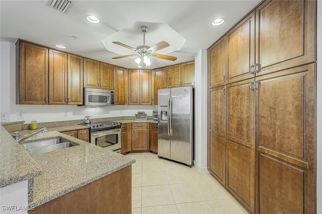 kitchen with kitchen peninsula, appliances with stainless steel finishes, light stone countertops, ceiling fan, and sink