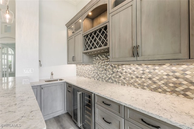 kitchen with wine cooler, tasteful backsplash, light stone counters, pendant lighting, and sink