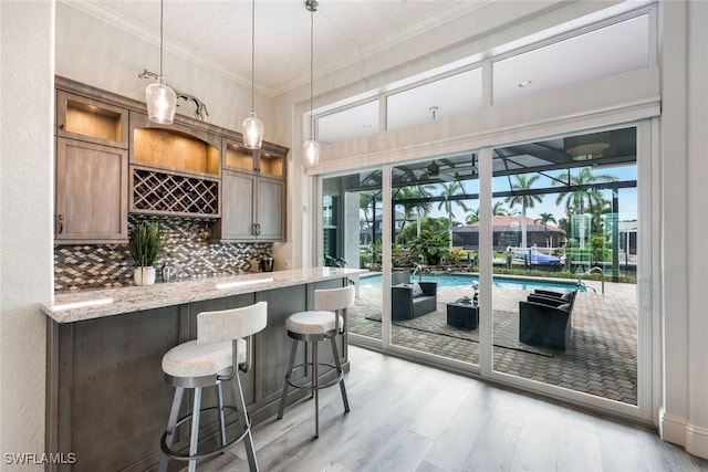 bar with backsplash, light stone countertops, light wood-type flooring, pendant lighting, and crown molding