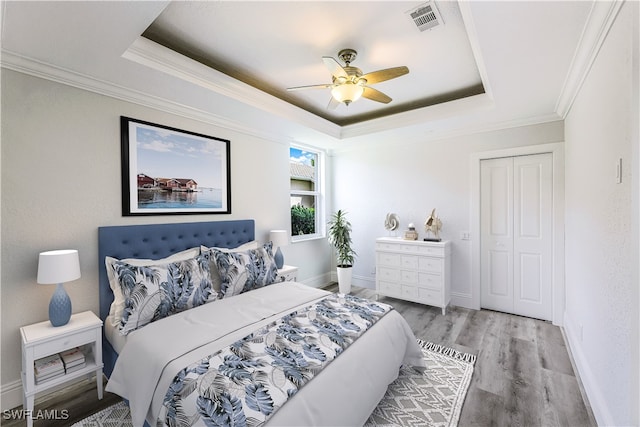 bedroom featuring a closet, a raised ceiling, light wood-type flooring, and ceiling fan