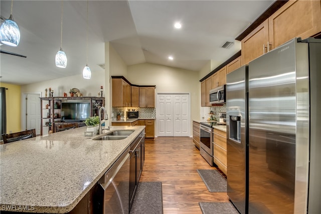 kitchen featuring pendant lighting, an island with sink, vaulted ceiling, backsplash, and appliances with stainless steel finishes