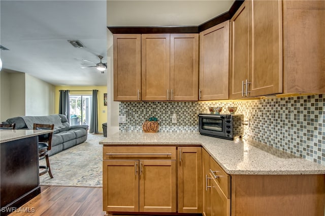 kitchen featuring ceiling fan, backsplash, light stone counters, and dark wood-type flooring